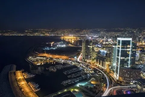 Nighttime aerial view of illuminated coastal city with harbor, buildings, and water reflections