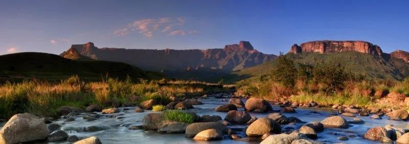 Mountain landscape with river, golden grassland, and dramatic cliff formations at sunset