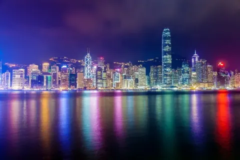 Nighttime Hong Kong skyline with colorful neon-lit buildings reflected in water