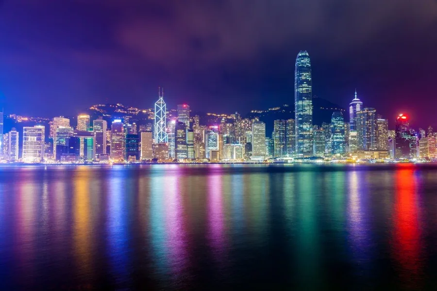 Nighttime Hong Kong skyline with colorful neon-lit buildings reflected in water
