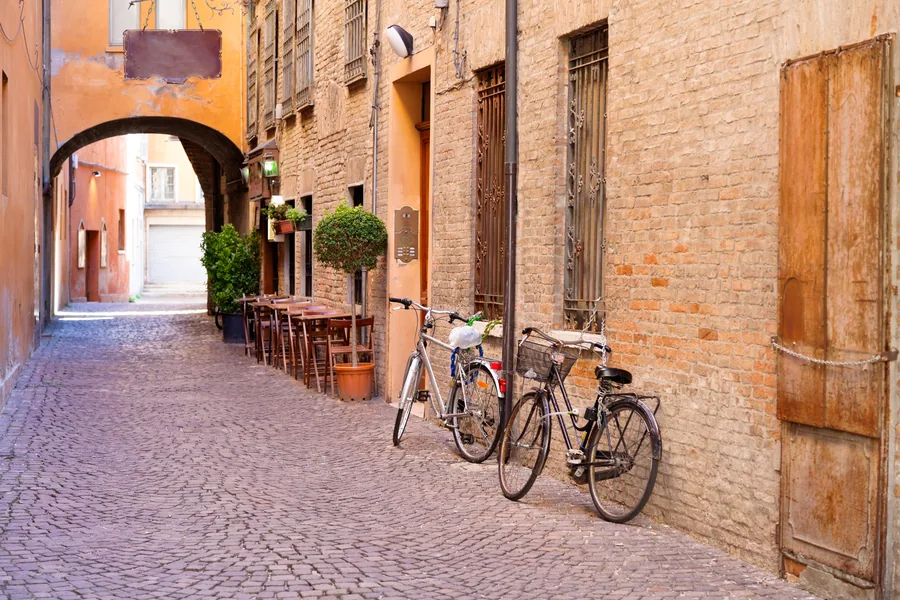 Narrow Italian alley with terracotta buildings, arched passage, bicycles, and cobblestone street.