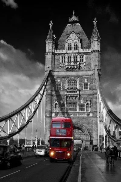 Black and white Tower Bridge with red London bus crossing the bridge against dramatic sky