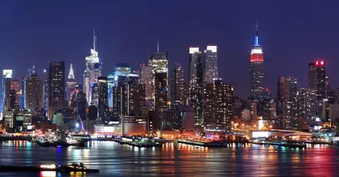 Night cityscape with illuminated buildings reflected in water, purple twilight sky