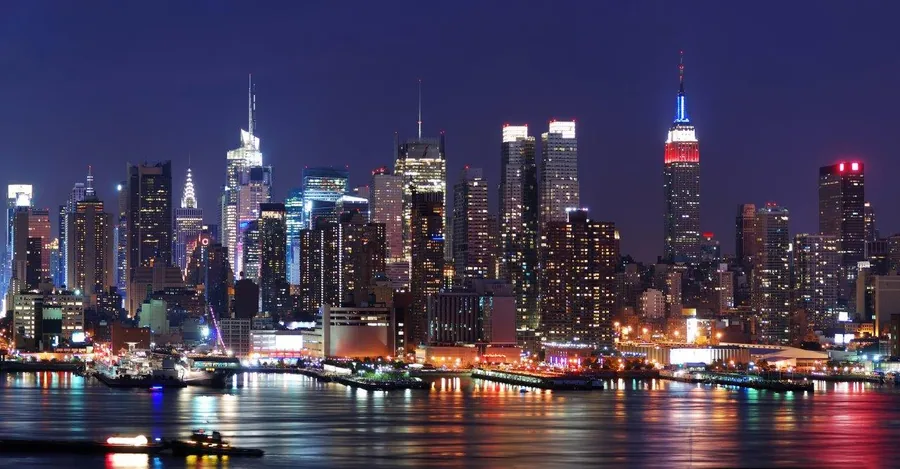 Night cityscape with illuminated buildings reflected in water, purple twilight sky