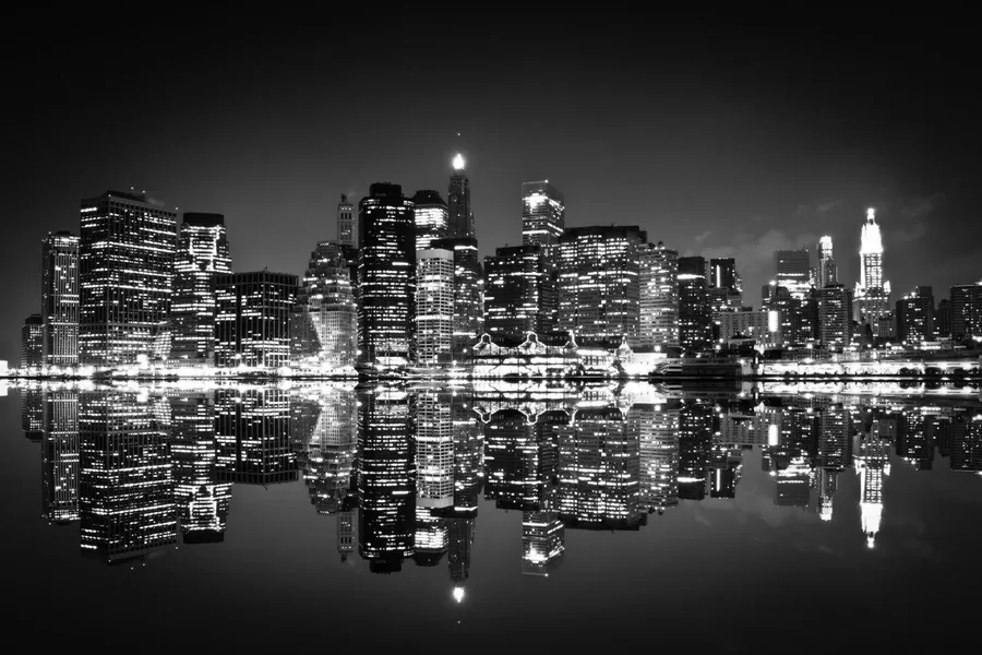 Night cityscape with lit buildings reflected in dark water, black and white photography style