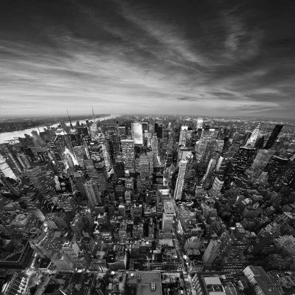 Black and white aerial photograph of Manhattan's dense urban skyline with river and clouds.