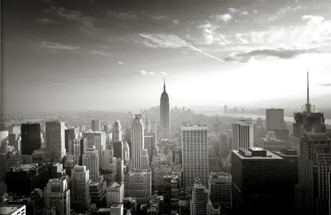 Black and white aerial view of New York City skyline with Empire State Building and dense skyscrapers under cloudy sky.