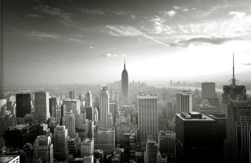 Black and white aerial view of New York City skyline with Empire State Building and dense skyscrapers under cloudy sky.