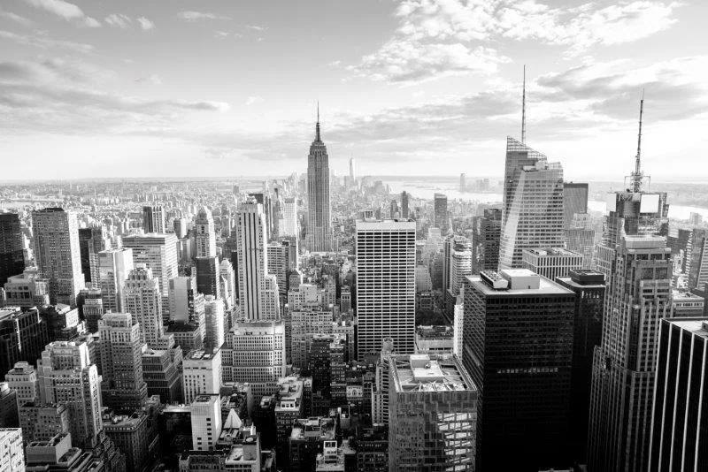 Black and white aerial photograph of Manhattan skyline with Empire State Building centered among tall buildings and clouds
