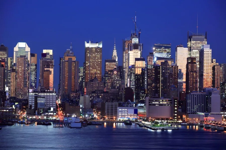 NYC Manhattan skyline at dusk with lit buildings reflected in blue water against twilight sky