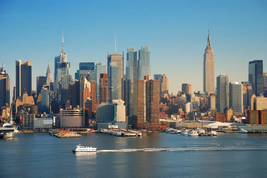 New York City skyline featuring Empire State Building, Hudson River, and boats on a clear blue day.
