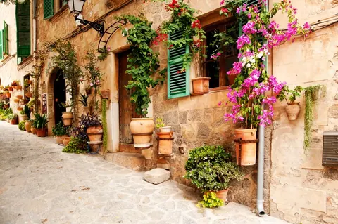 Tuscan village alleyway with terracotta pots, magenta flowers, and weathered stone walls