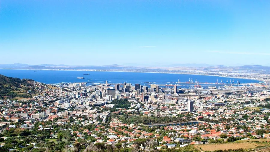 Aerial view of Melbourne's skyline with blue bay, residential suburbs, and distant mountains under clear sky