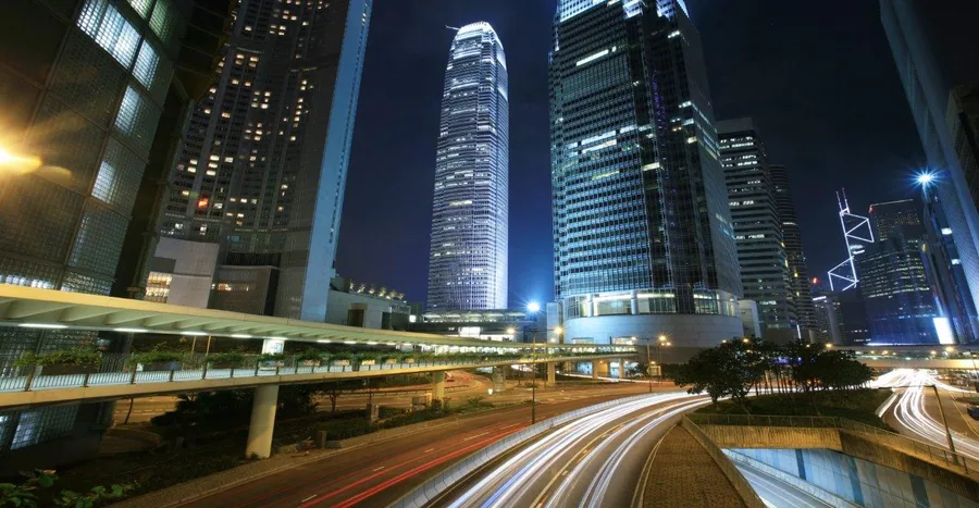 Night cityscape with glowing skyscrapers, highways, and light trails creating urban energy.