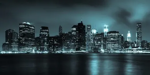 Night cityscape with illuminated buildings reflected in dark water under stormy sky