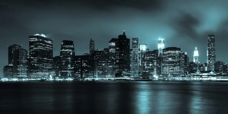 Night cityscape with illuminated buildings reflected in dark water under stormy sky