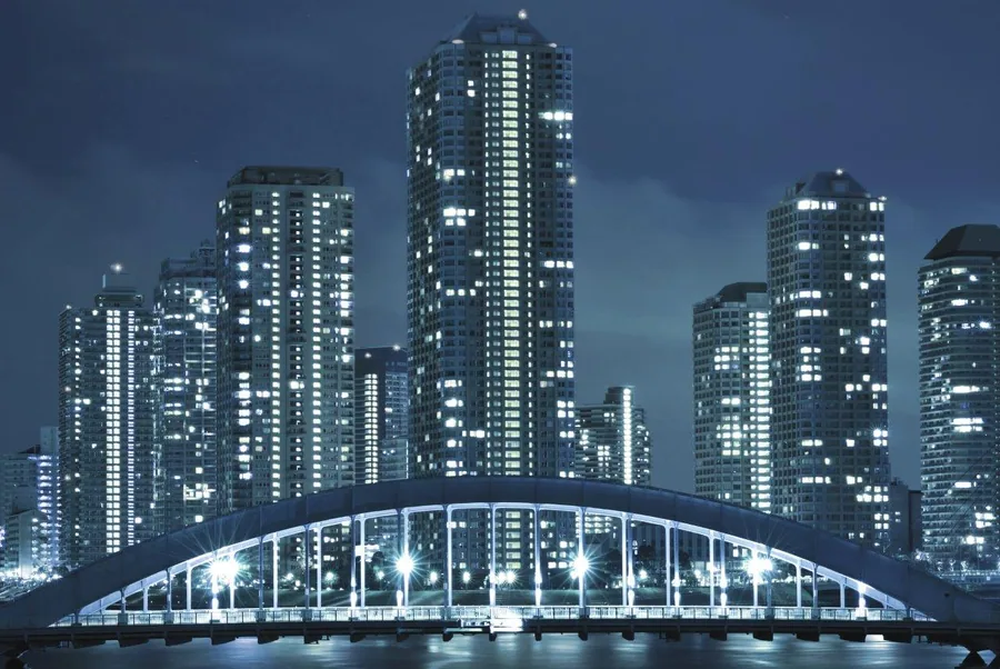 Nighttime city skyline with lit high-rise buildings and illuminated bridge over water at dusk