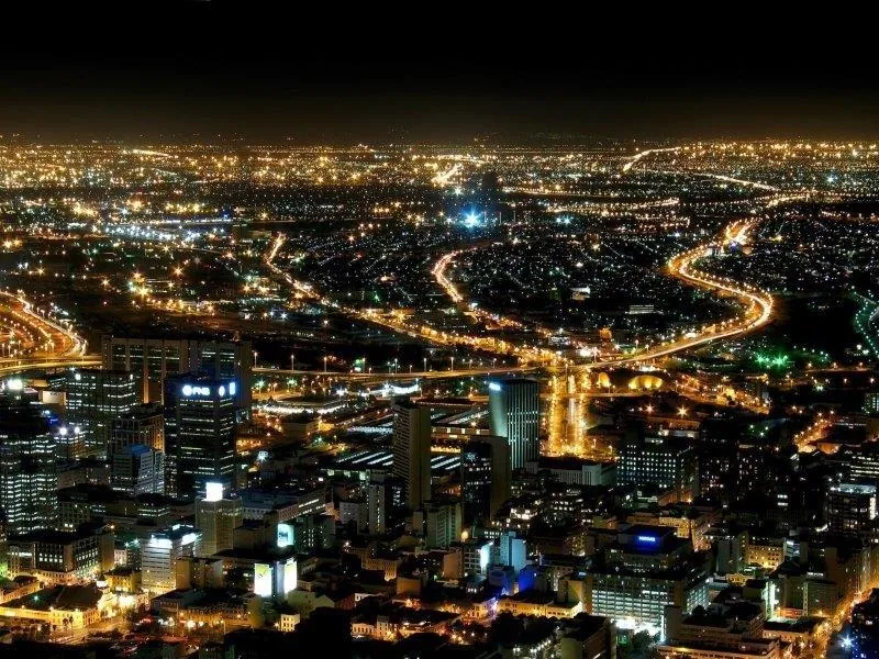 Aerial night view of a sprawling city with golden highway lights and glowing buildings against dark sky