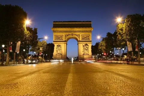 Arc de Triomphe at dusk on illuminated Champs-Élysées with tree-lined avenue and street lights