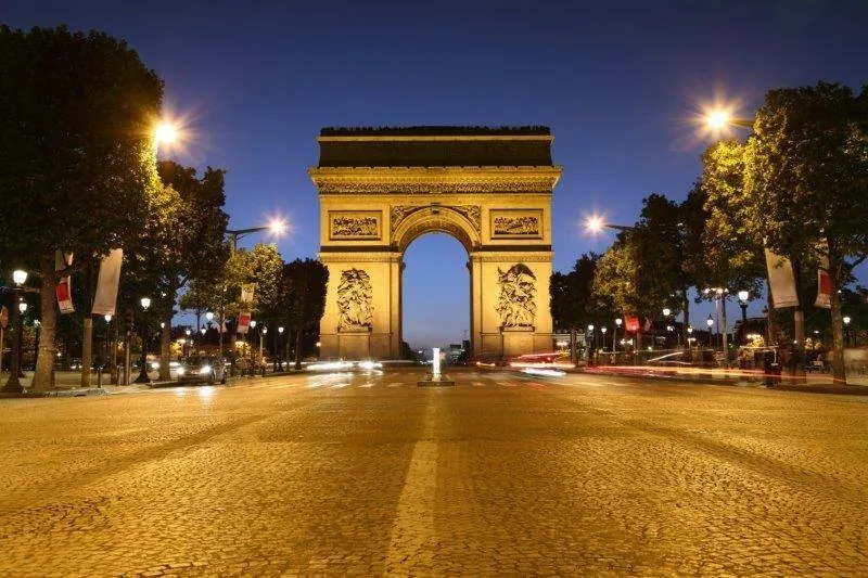Arc de Triomphe at dusk on illuminated Champs-Élysées with tree-lined avenue and street lights