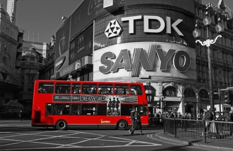 Black and white London street scene with red double-decker bus and TDK/Sanyo advertisement screens