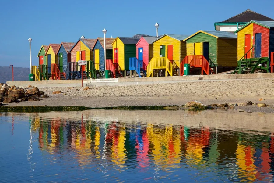 Colorful beach huts with red, yellow, green, and blue painted wooden structures reflected in water.