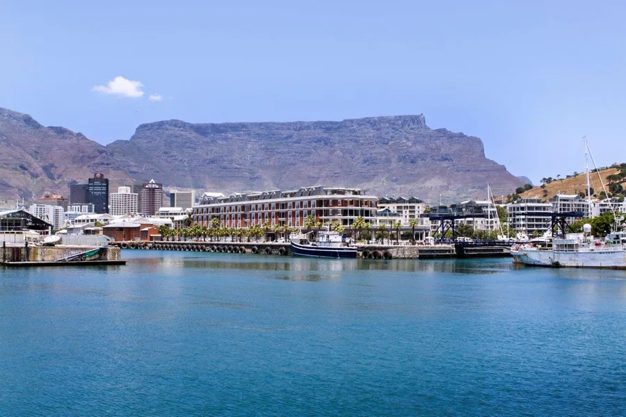 Cape Town waterfront with Table Mountain backdrop, modern buildings, boats, and blue harbor water.