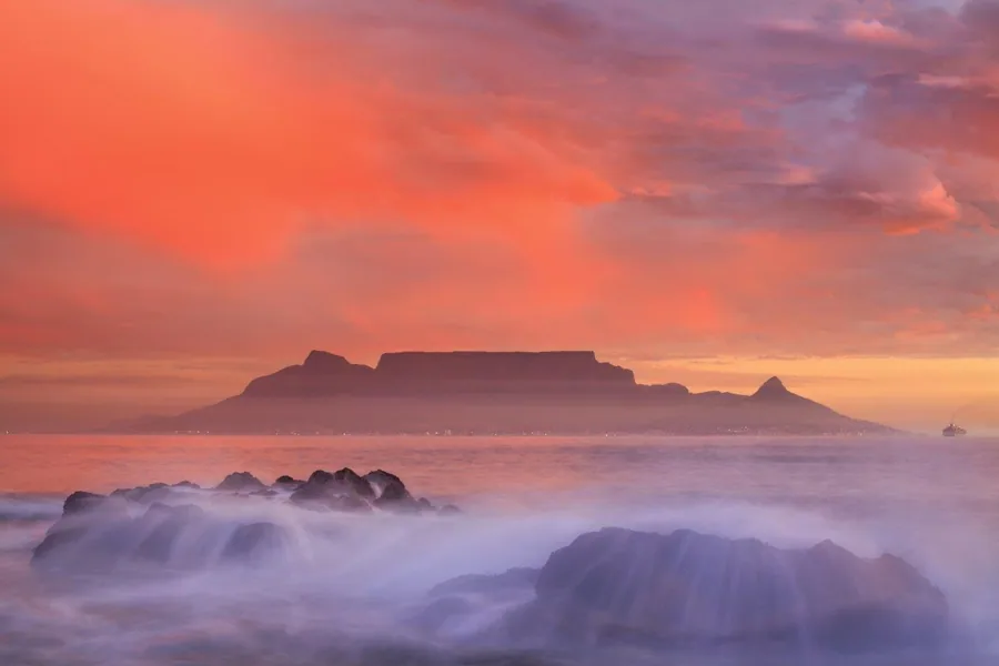 Table Mountain at sunrise with orange sky, waves, and rocky coastline