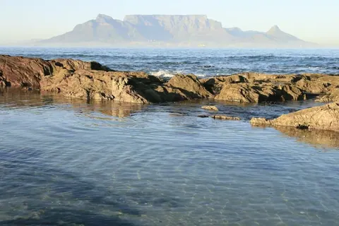 Rocky beach with calm blue ocean and flat-topped mountain in the distance under clear sky