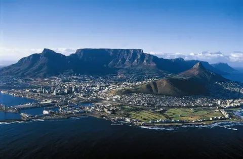 Aerial view of Cape Town with Table Mountain, city buildings, and blue ocean waters.