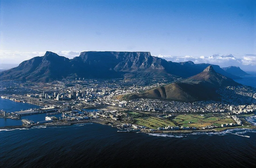 Aerial view of Cape Town with Table Mountain, city buildings, and blue ocean waters.