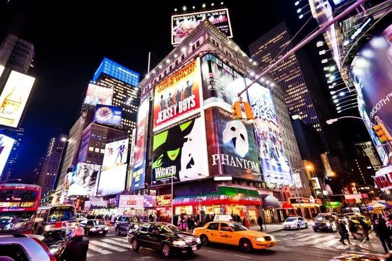 Nighttime Times Square with illuminated theatre signs, yellow taxis, and colorful digital billboards.