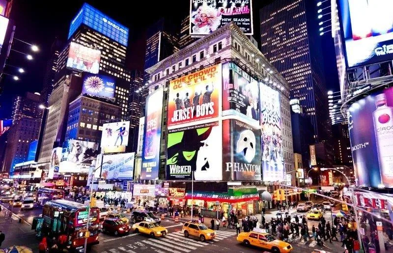 Night scene of Times Square with glowing digital billboards, yellow cabs, and crowds of people crossing streets