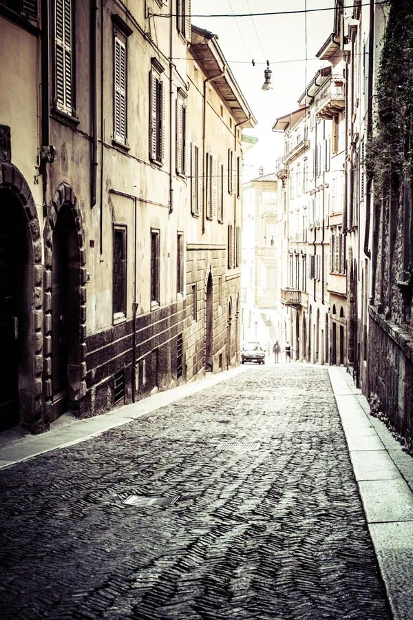 Narrow Italian street with cobblestone path flanked by historic stone buildings and shuttered windows