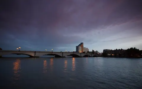 Evening cityscape with lit bridge over water, buildings and dramatic sky at dusk