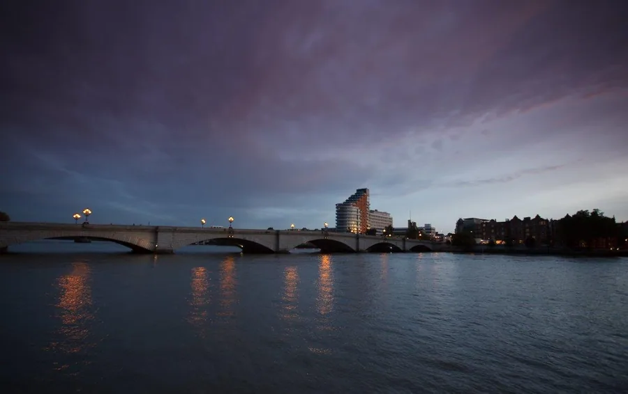Evening cityscape with lit bridge over water, buildings and dramatic sky at dusk