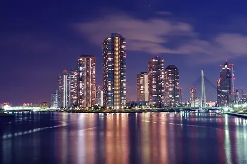Night cityscape with glowing skyscrapers reflected in still water under purple twilight sky