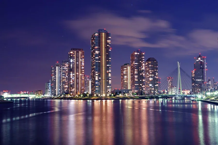 Night cityscape with glowing skyscrapers reflected in still water under purple twilight sky