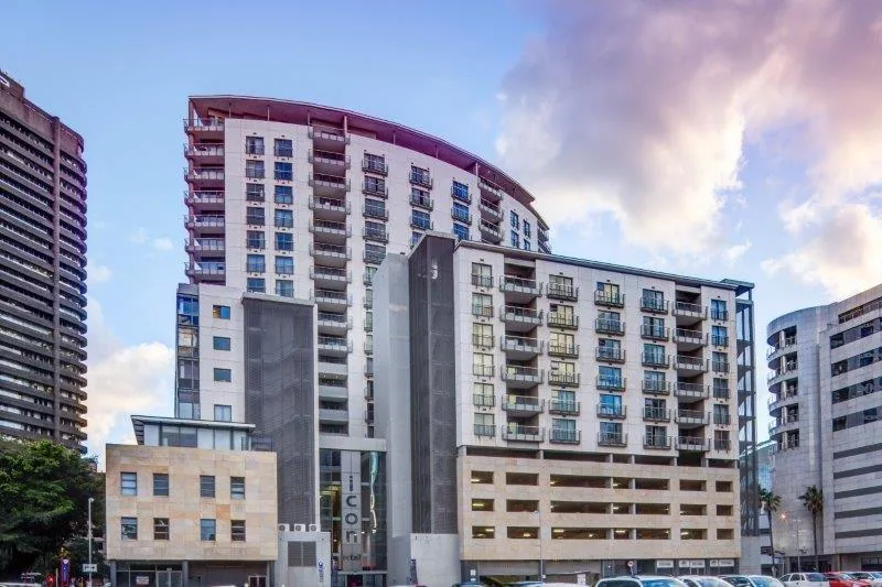 Modern residential apartment buildings with curved architecture, blue windows, and contemporary design against a cloudy sky.