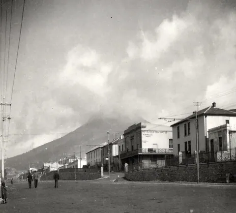 Black and white vintage street scene with historic buildings and a looming mountain in the background