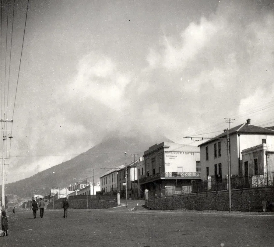 Black and white vintage street scene with historic buildings and a looming mountain in the background