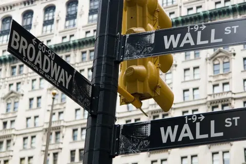 Wall Street and Broadway street signs with yellow traffic light and historic buildings