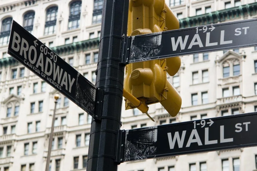 Wall Street and Broadway street signs with yellow traffic light and historic buildings