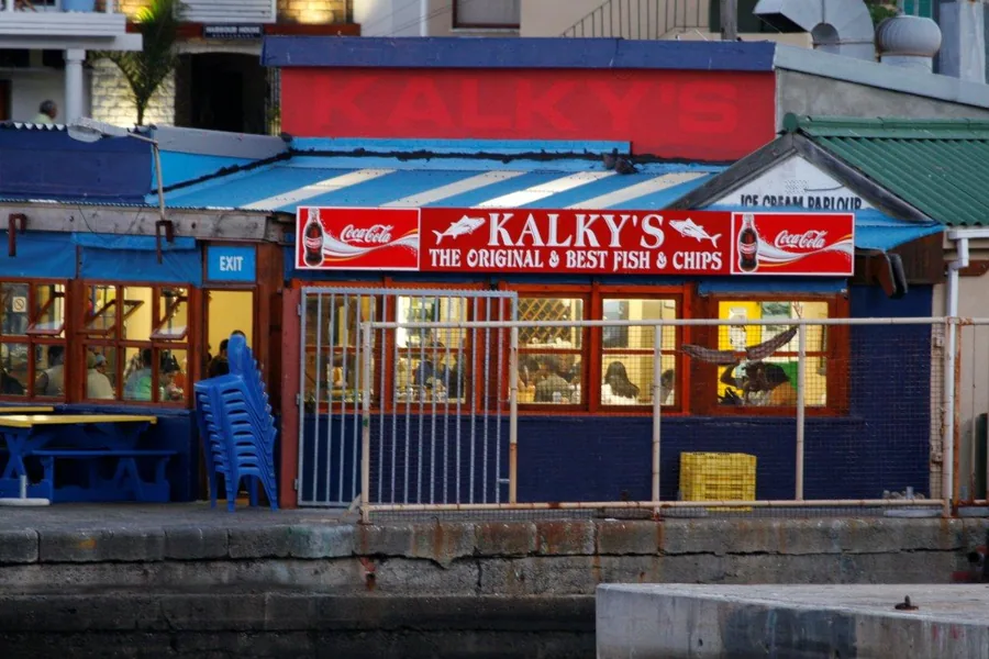 Colorful waterfront fish and chips shop with Kalky's storefront, blue railings, and coastal architecture