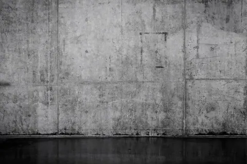 Aged concrete wall panels with visible seams, stains, and weathered surface texture.