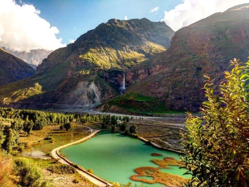 Mountain valley with turquoise lake, waterfall, and coniferous forest under blue sky
