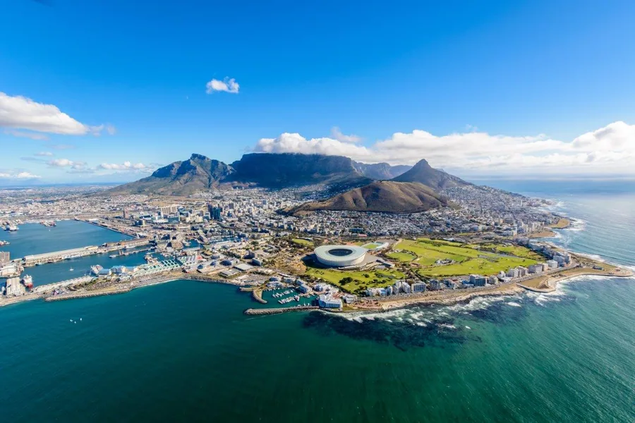 Aerial photograph of Cape Town with Table Mountain, city skyline, and turquoise ocean waters under blue sky.