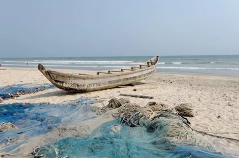Abandoned wooden fishing boat with blue nets on sandy beach by calm sea