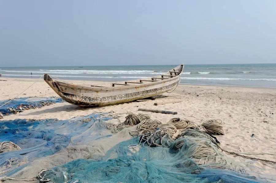 Abandoned wooden fishing boat with blue nets on sandy beach by calm sea