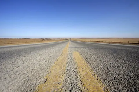 Long straight highway with yellow center line disappearing into desert horizon under clear blue sky